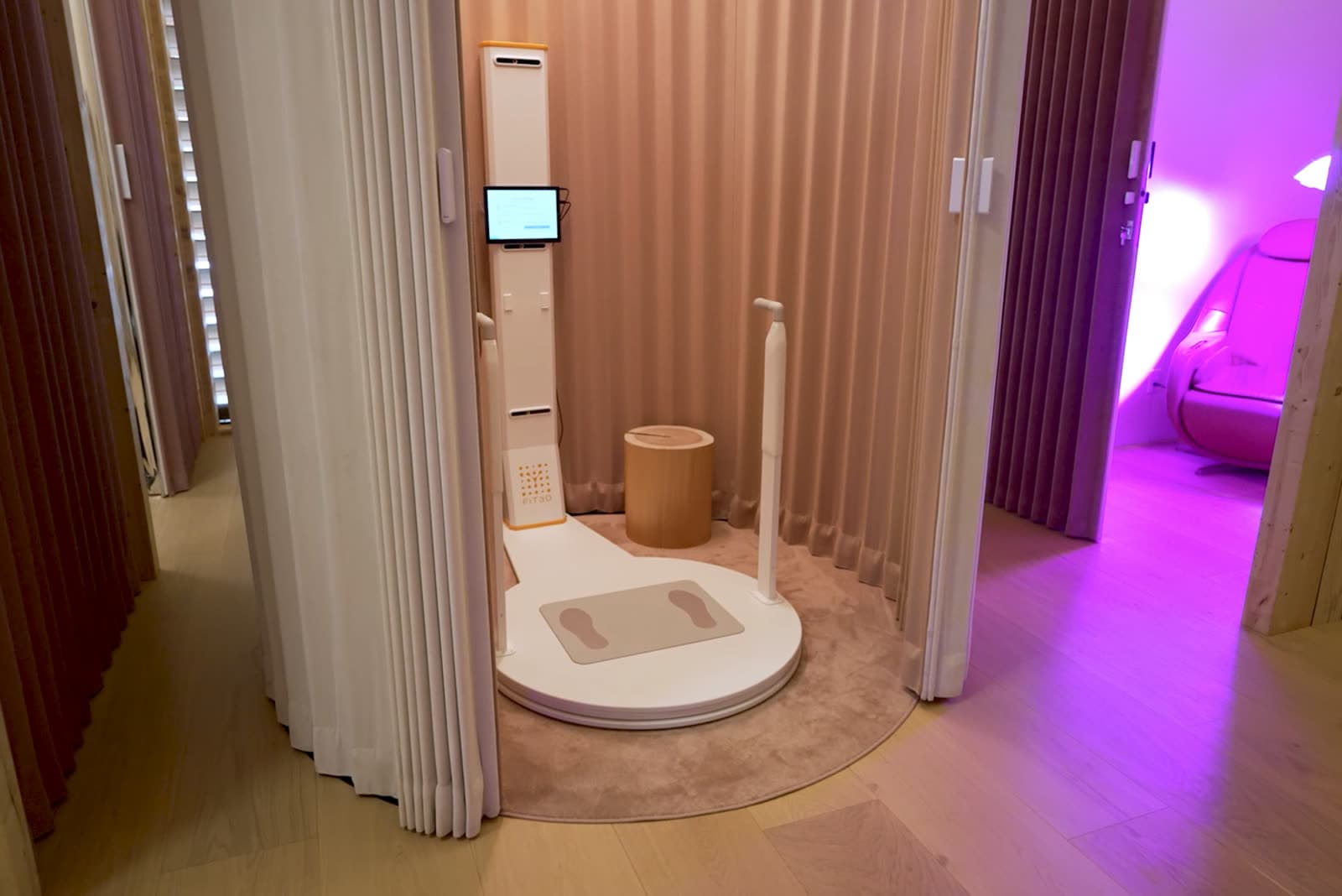 The body-composition scanner in its curtained bay at Circadium, the violet therapy room beyond